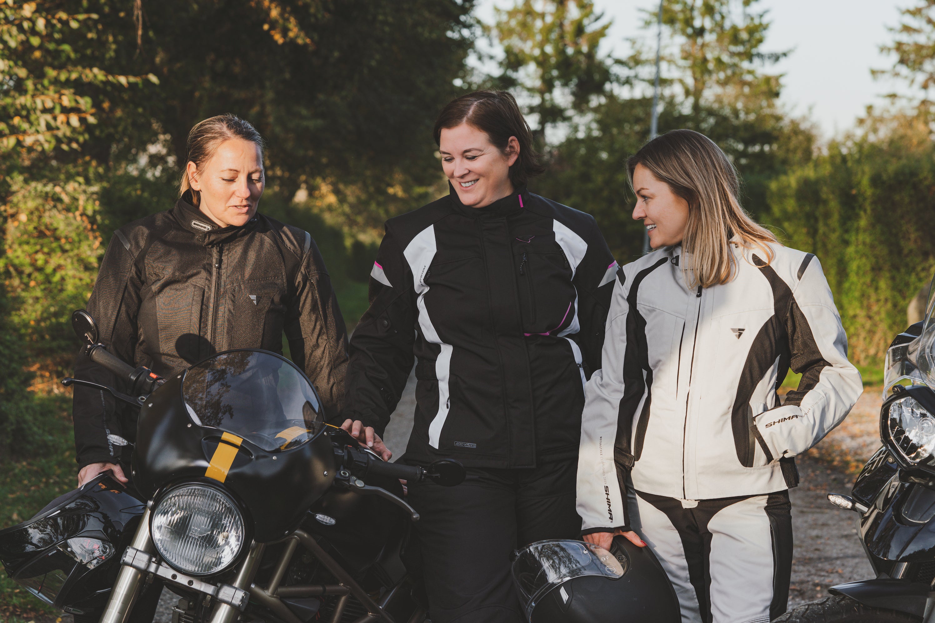 Three women wearing lady motorcycle clothes standing by motorcycles and chatting
