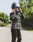 Person wearing a black helmet and green jacket on a road with trees in the background