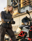 A blong young woman standing by her motorcycle wearing Black and grey lumberjack style women's motorcycle shirt from Shima