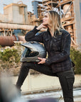 A blond young woman dreaming while holding her motorcycle helmet wearing Black and grey lumberjack style women's motorcycle shirt from Shima