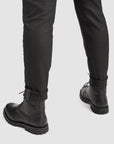 Person wearing black leather boots and black pants on a white background