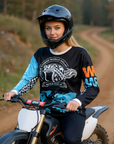 a woman on a dirt bike wearing a black and blue jersey with visible branding in a forest setting