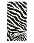 A rectangular beach towel featuring a bold black and white zebra stripe pattern, with the brand name 'Motogirl' printed in a stylized black font at the bottom, set against a plain white background.