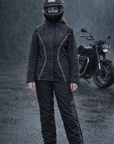 Person wearing a black motorcycle helmet and raincoat standing in the rain with a motorcycle in the background.
