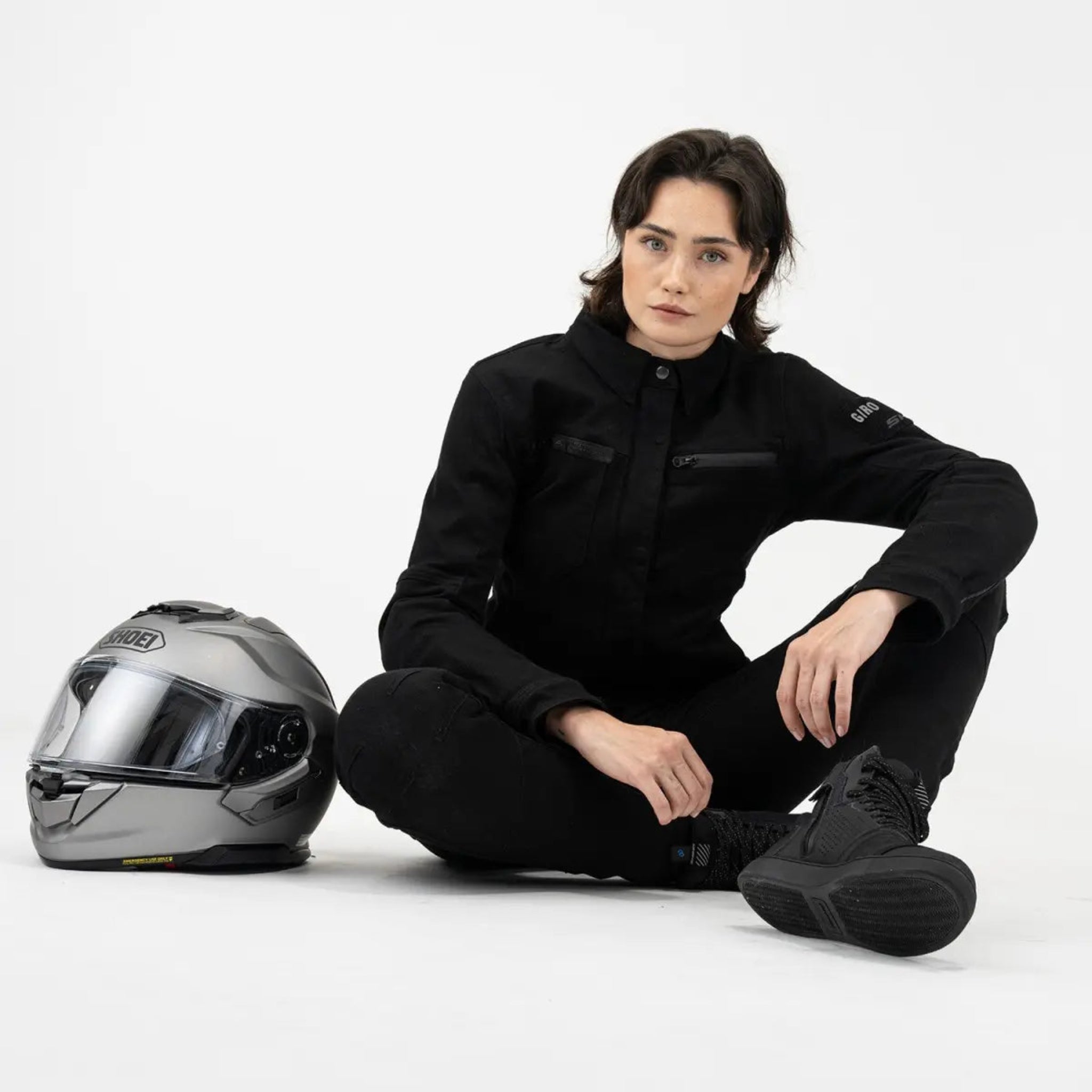 a motorcyclist sitting on the floor wearing black shirt looking lady motorcycle jacket with front pockets and zippers