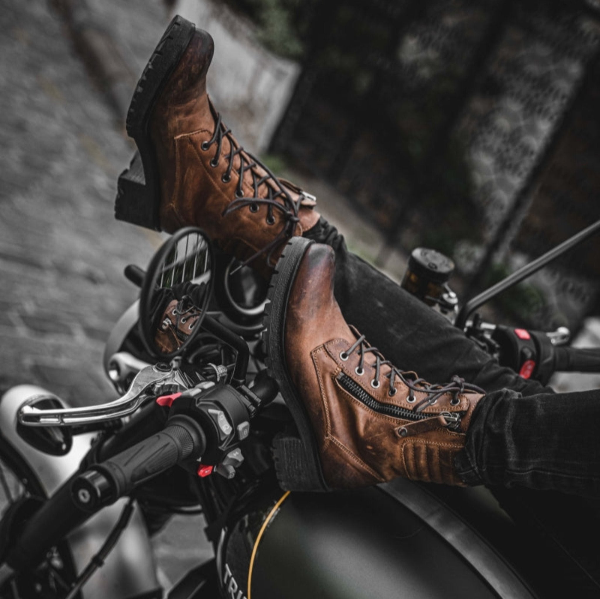 women's feet resting on motorcycle steering wheel, wearing brown leather mc boots