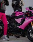 A woman wearing pink motorcycle trousers standing by a pink motorcycle