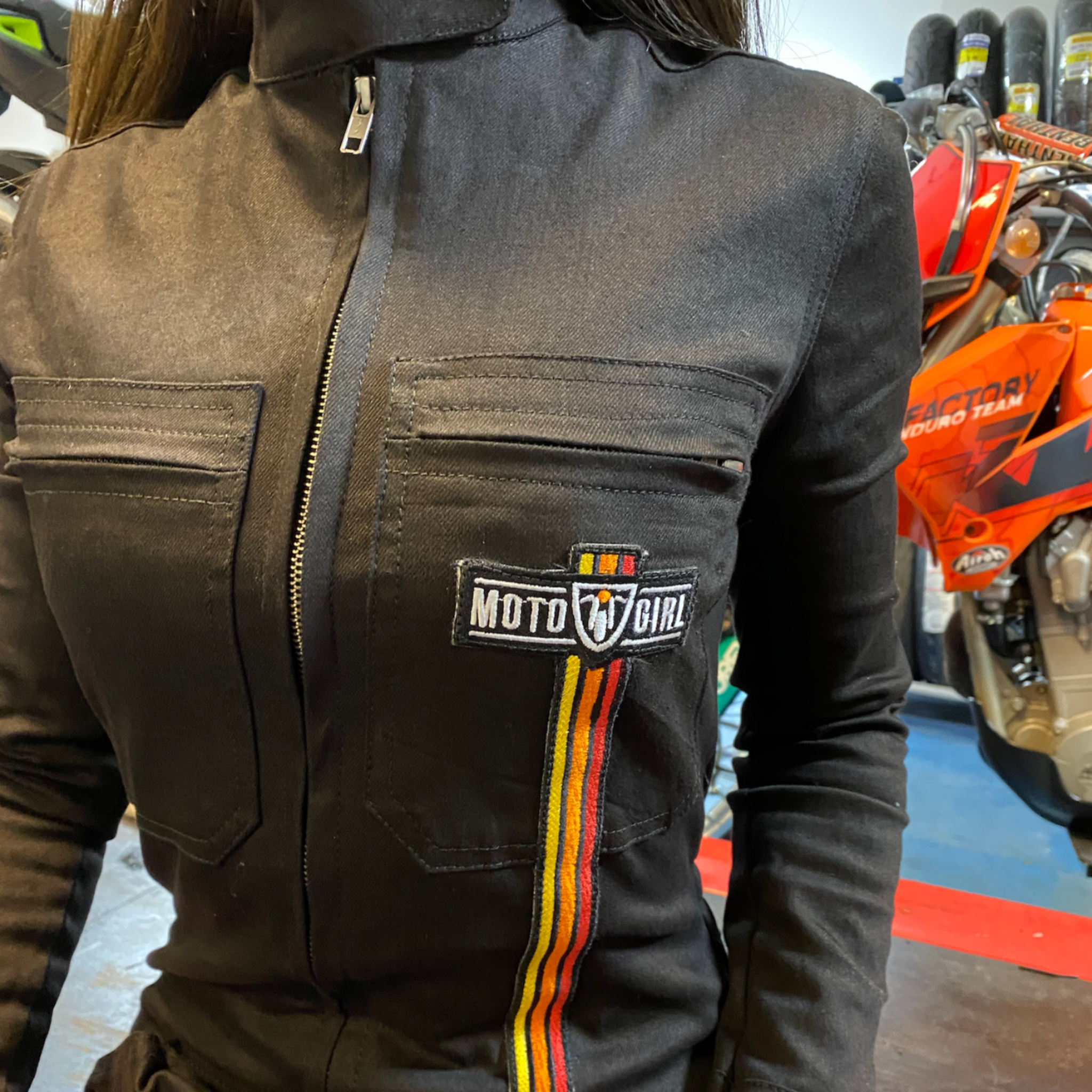 A close up of a woman's chest wearing black women's garage jumsuit with MotoGirl logo and stripe details