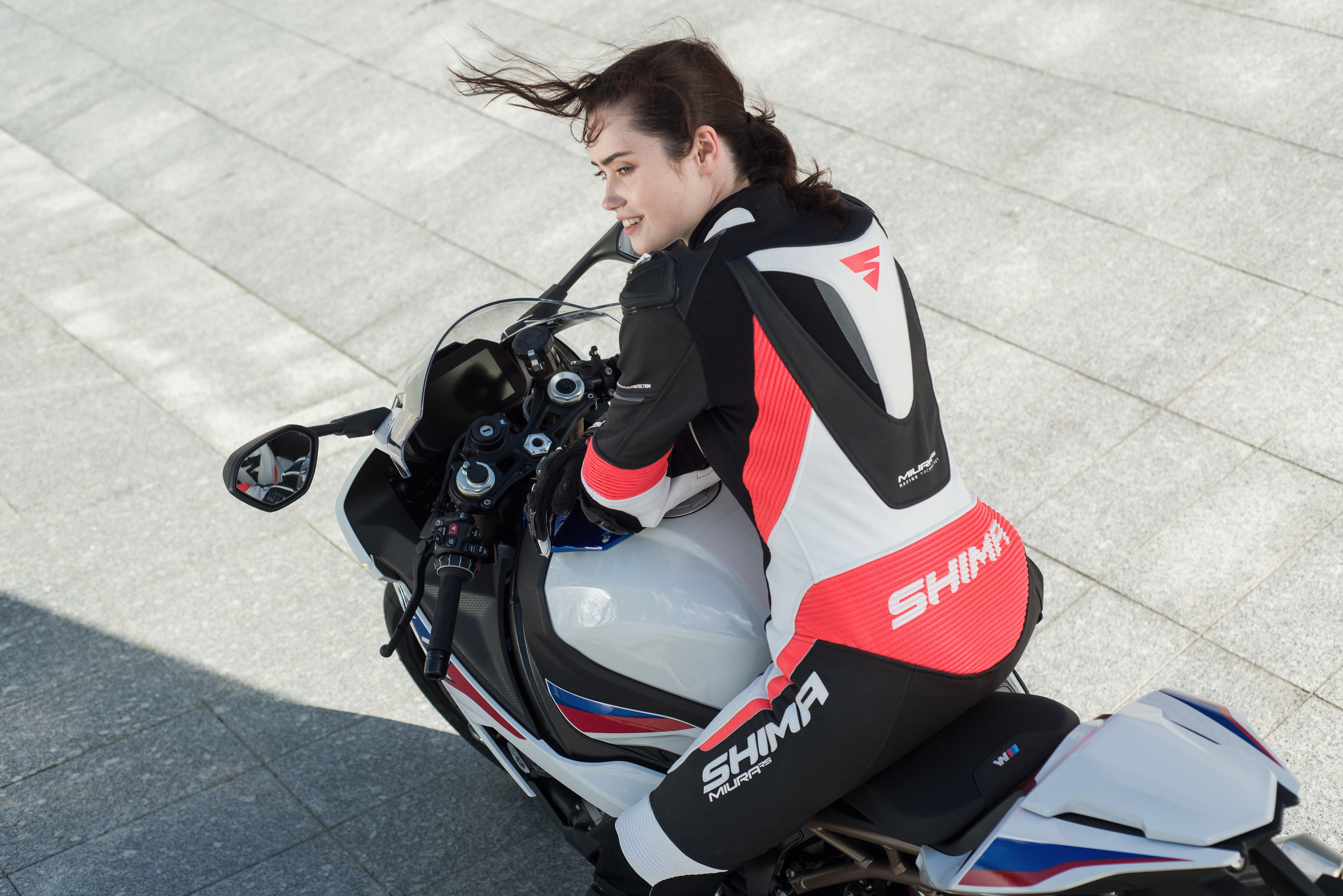 A woman on a motorcycle wearing Women&#39;s racing suit MIURA RS in black, white and fluo from Shima 