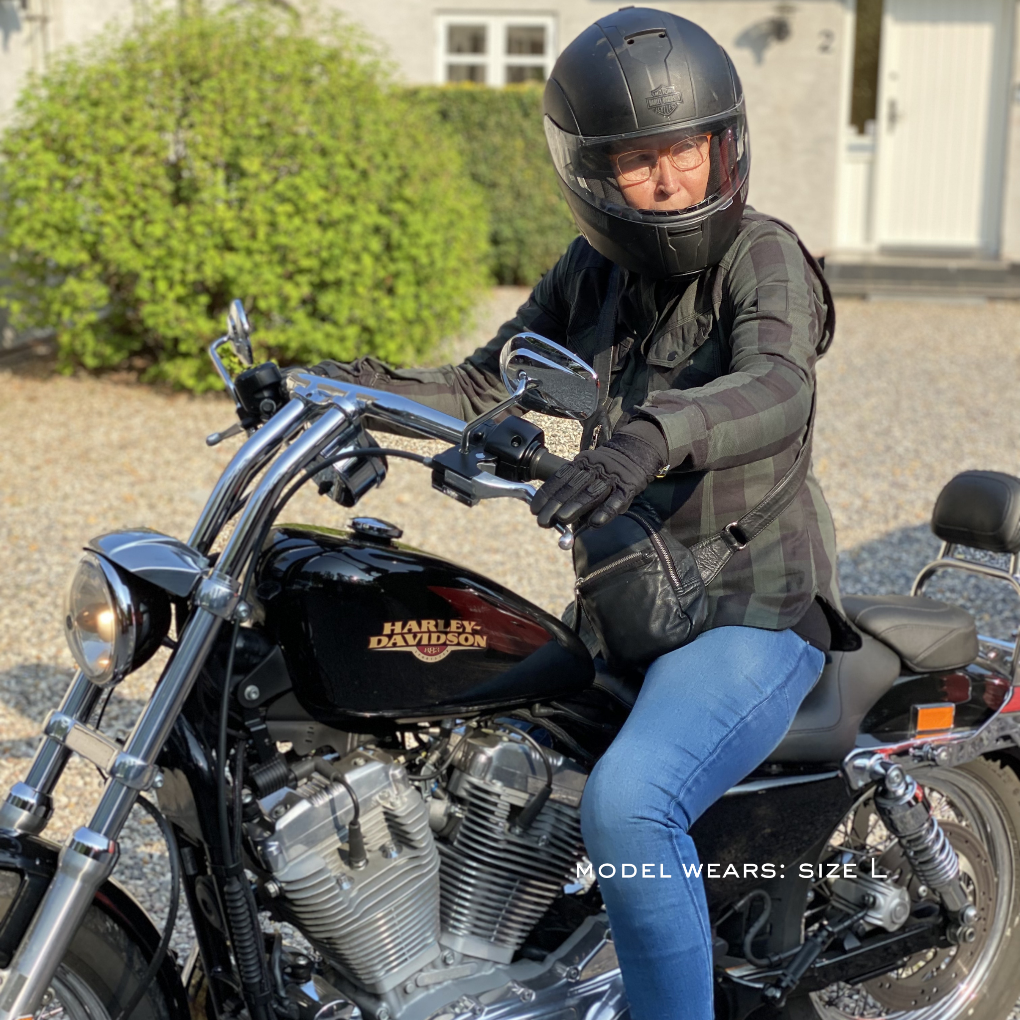 Person sitting on a Harley Davidson motorcycle wearing a helmet and plaid jacket.