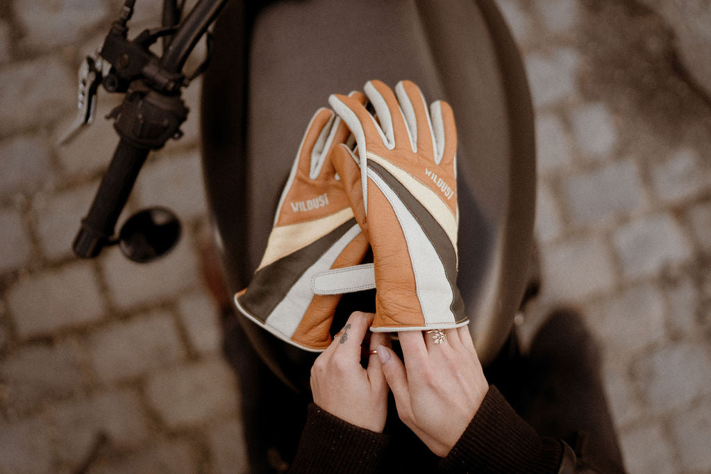 women&#39;s hands over a motorcycle gas tank while putting  on colourful leather gloves from WILDUST