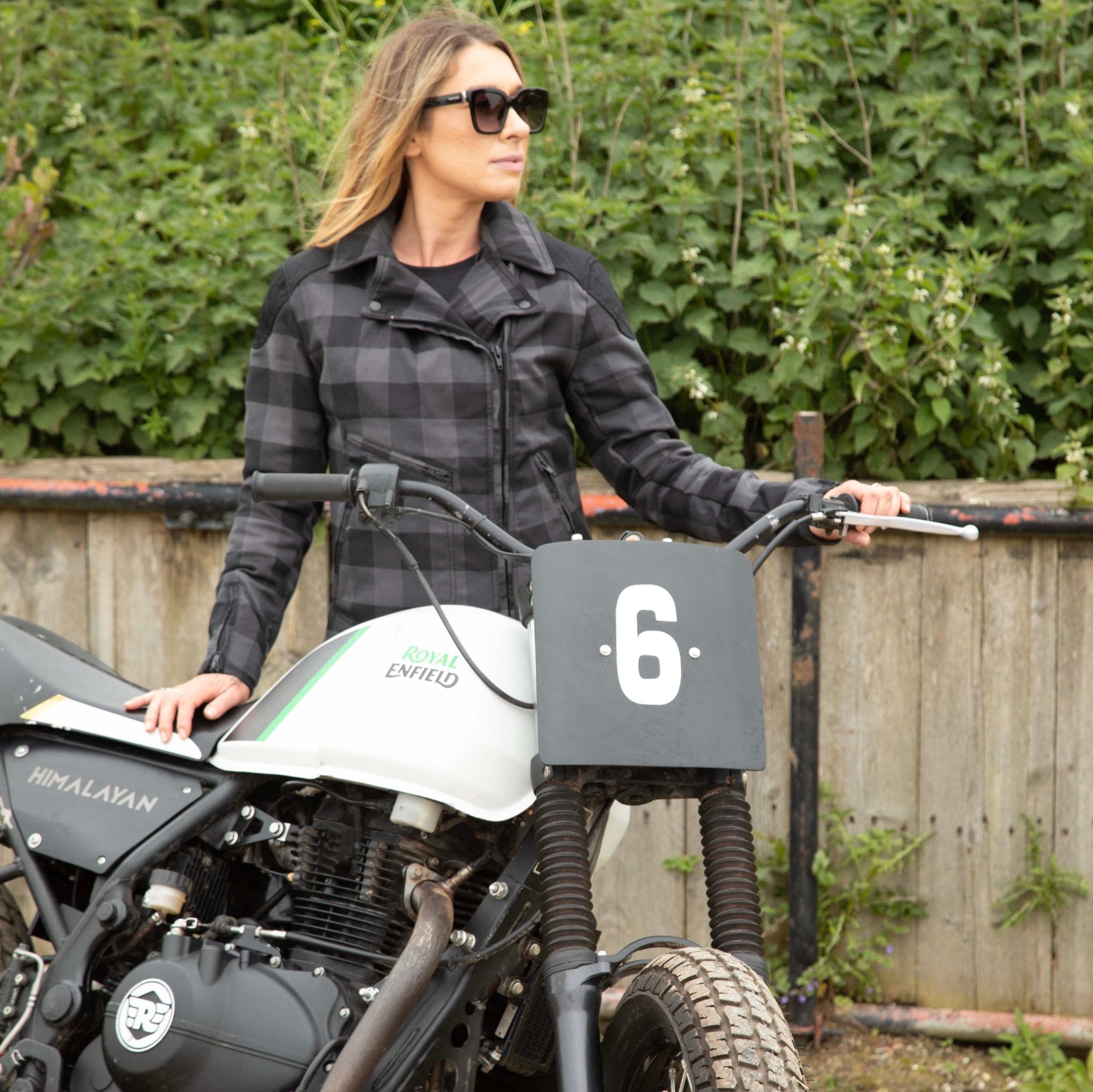 woman with sunglasses next to a motocross bike wearing a black & grey flannel style women's jacket 