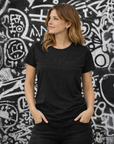 Woman wearing a black 'Moto Girl' t-shirt standing against a graffiti-covered wall.