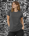 Woman wearing a gray t-shirt with 'Moto Lady' text against a black and white graffiti wall.