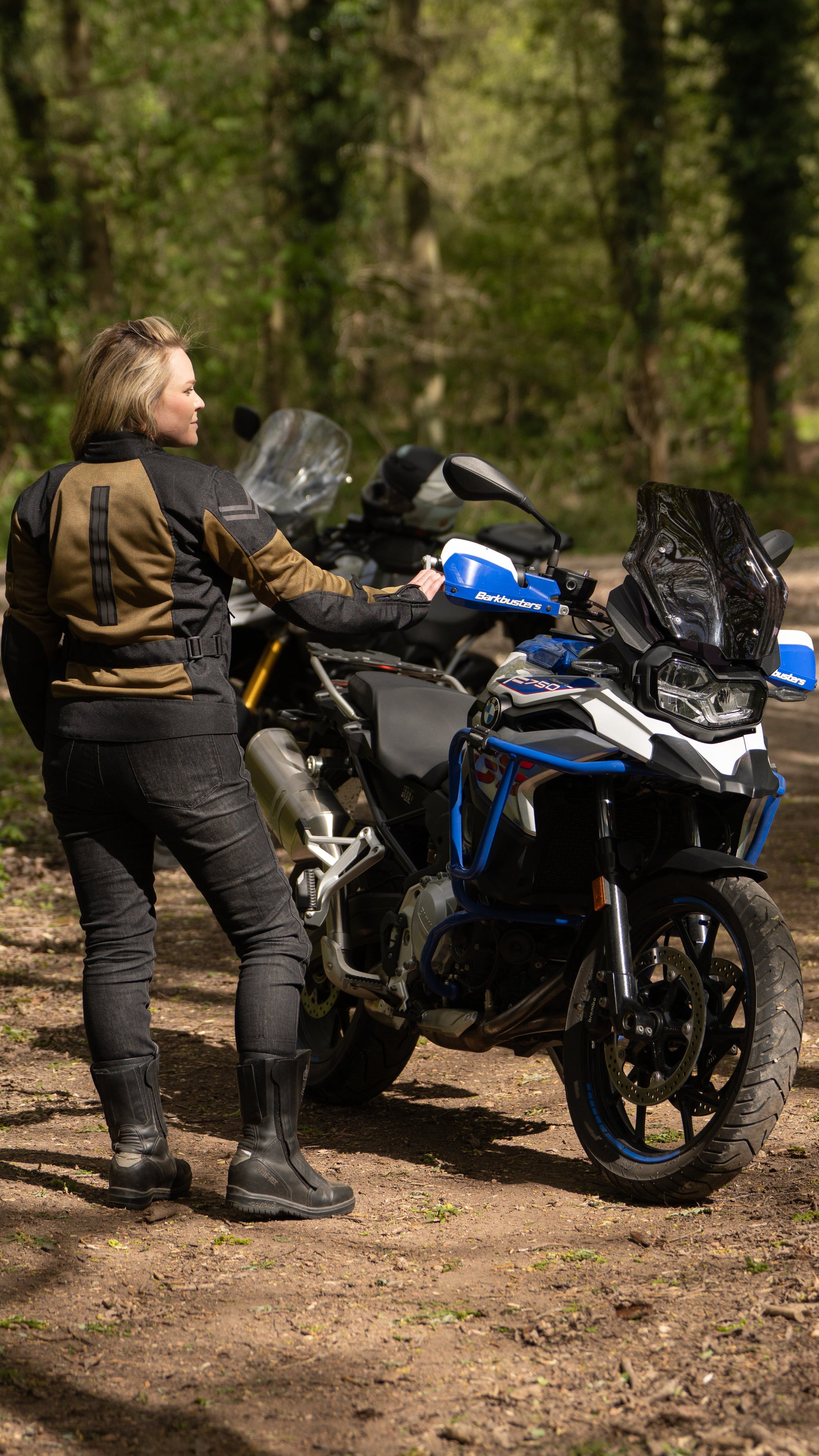 a blond woman standing by her big motorcycle wearing a black and gold mesh motorcycle jacket for women