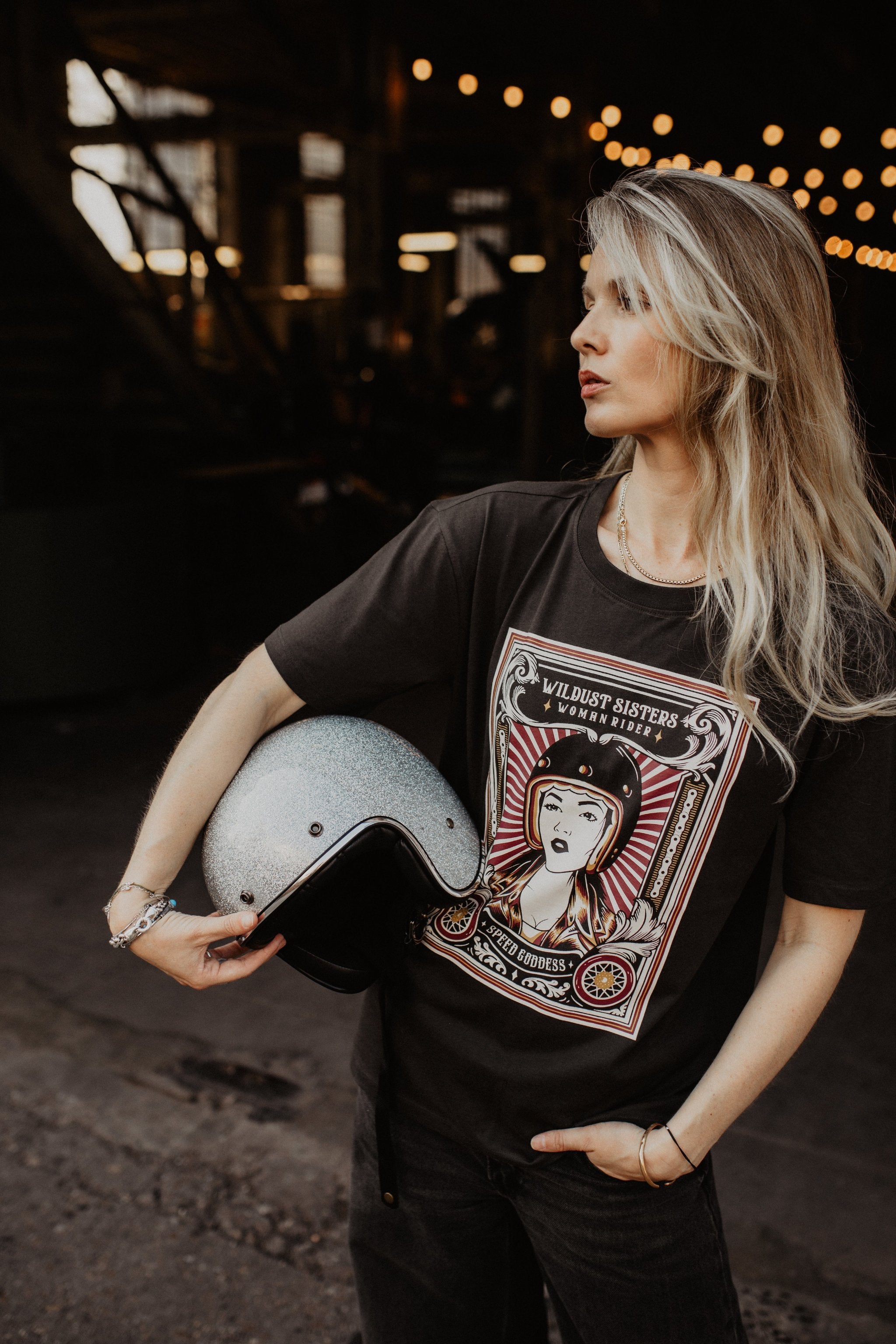 Woman with a Motorcycle helmet wearing a T-shirt with a women wearing a Motorcyclehelmet print and with the text "Wild dust sisters woman rider" and "Speed Goddess"