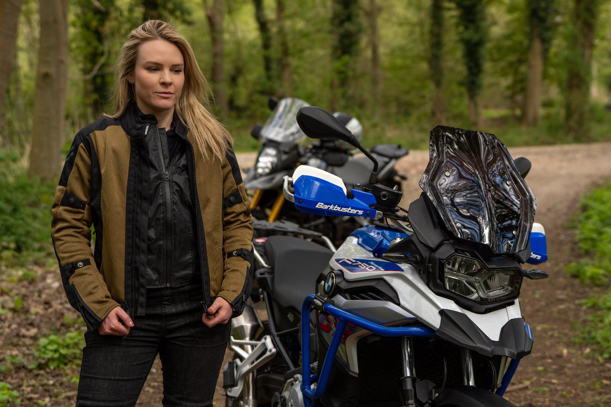 a blond woman standing by her big motorcycle wearing a black and gold mesh motorcycle jacket for women
