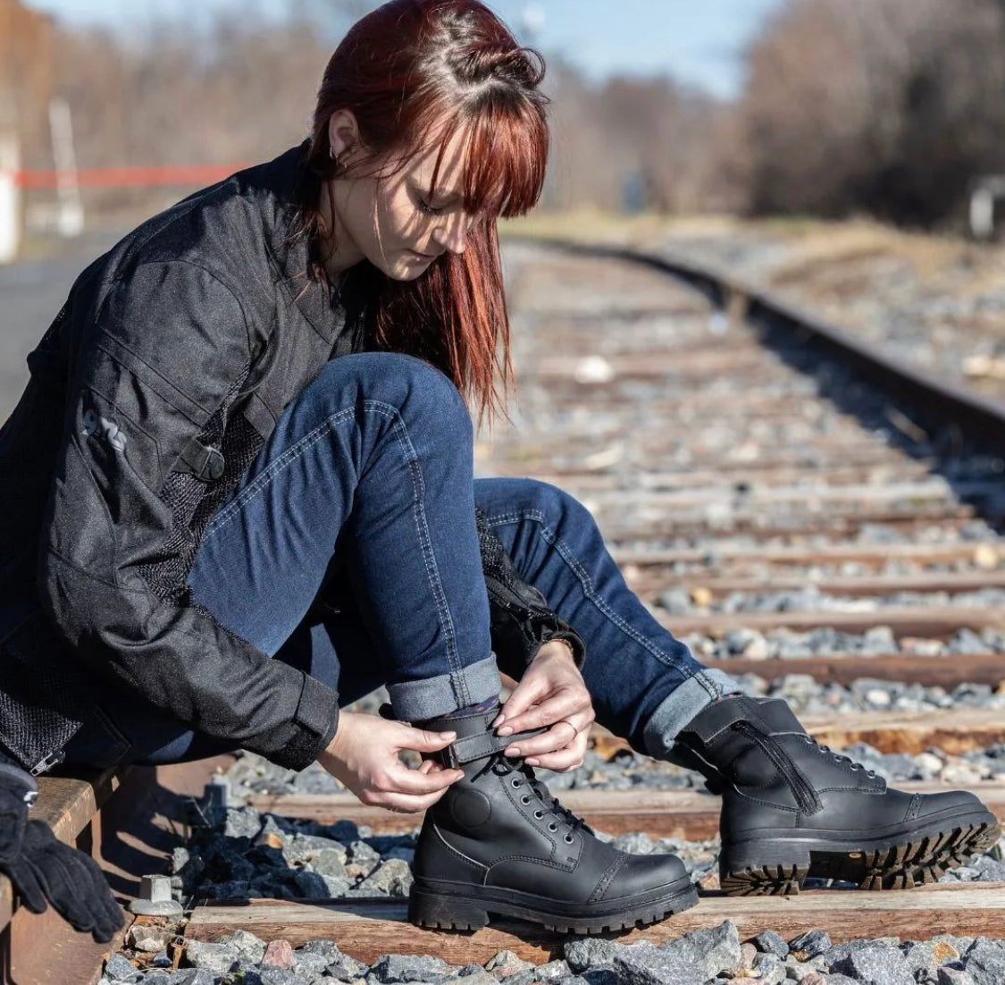 A woman sitting on the railway and closing her black motorcycle boots