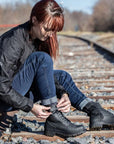 A woman sitting on the railway and closing her black motorcycle boots