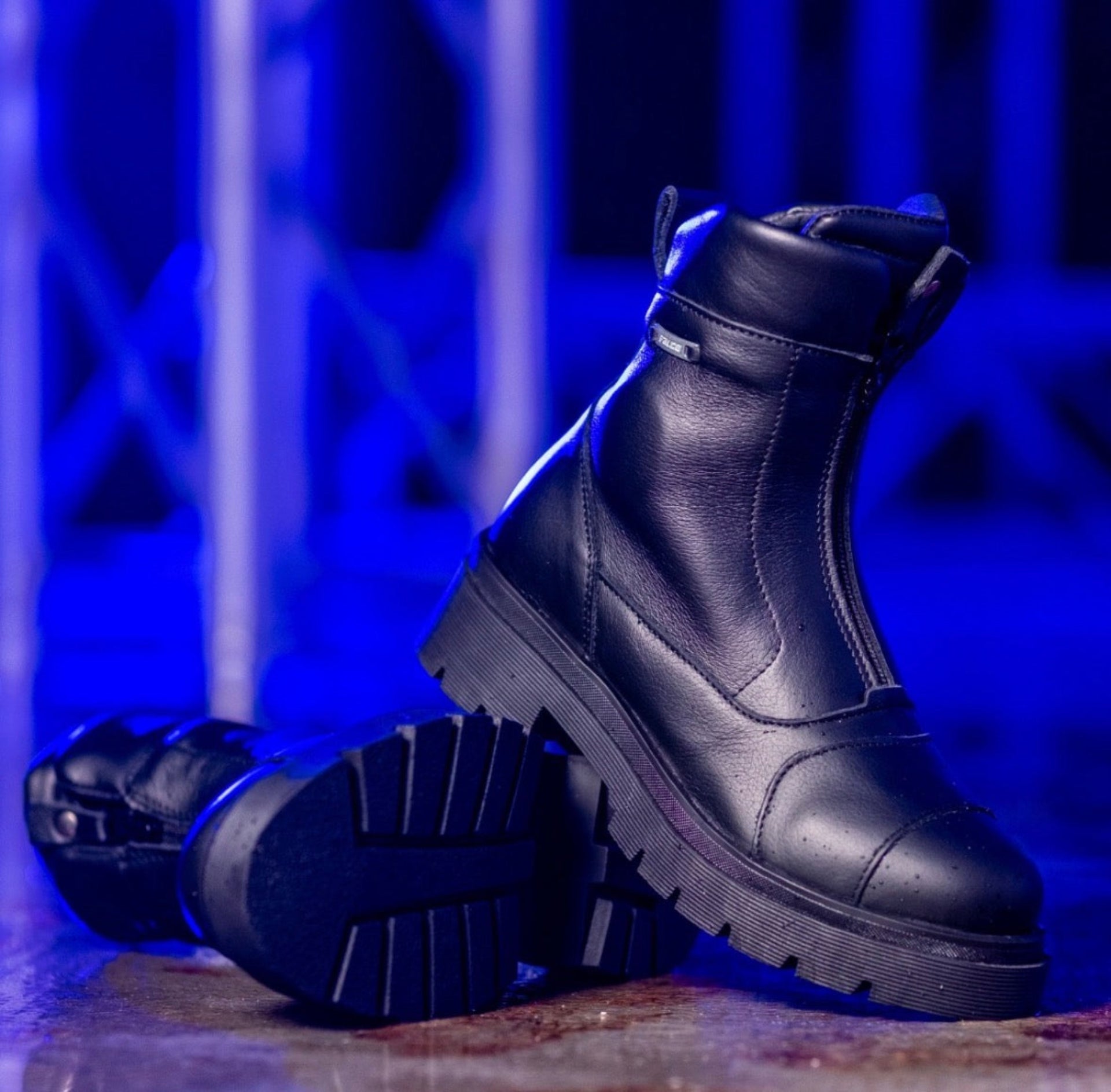Black leather boots with thick soles on a textured surface with blue lighting.
