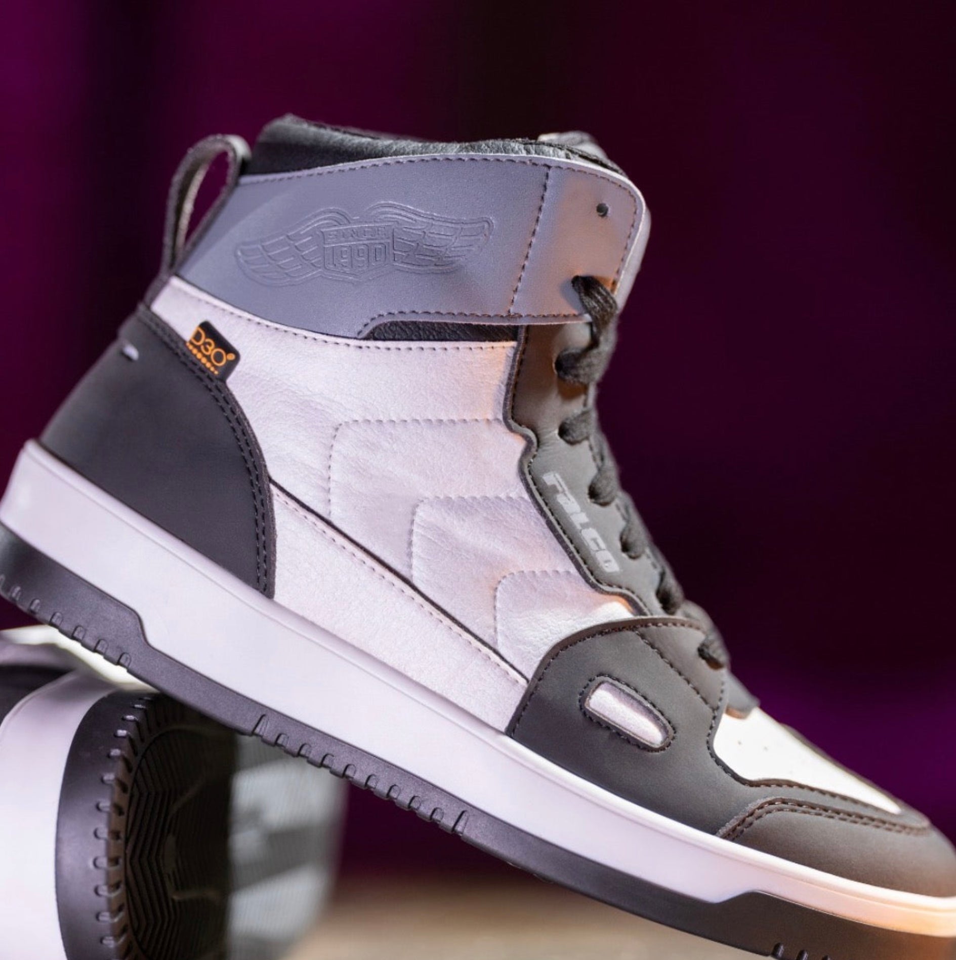 Gray and black high-top sneakers with white soles on a purple background