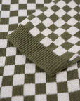 a sleeve of a knitted khaki green and white jumper with chessboard motives  from Wildust
