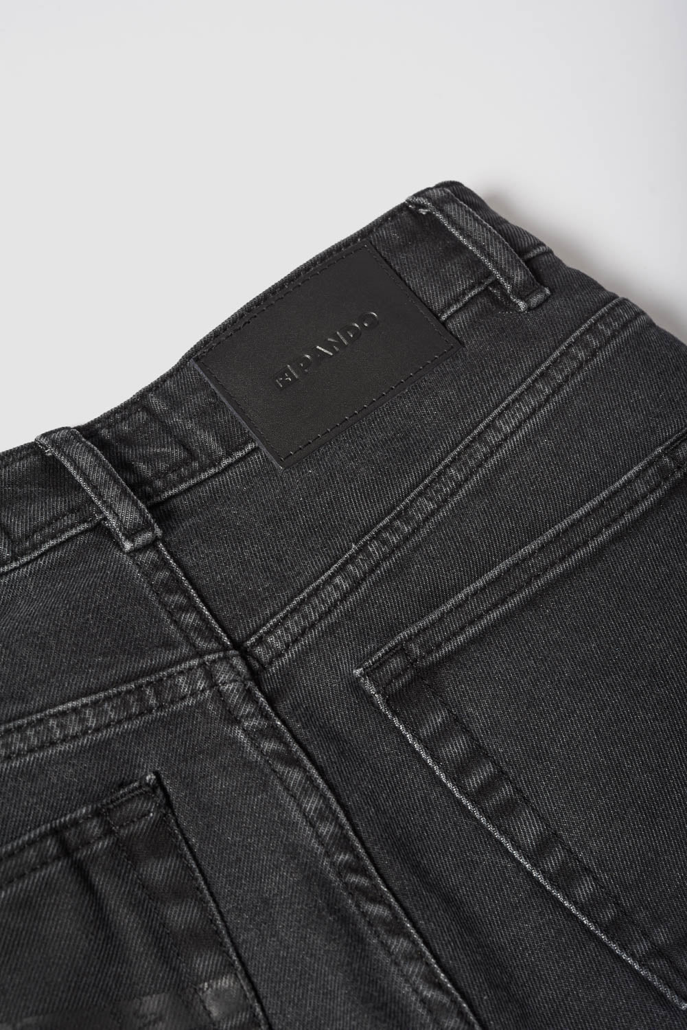 Close-up of black jeans with a brand label on a light gray background