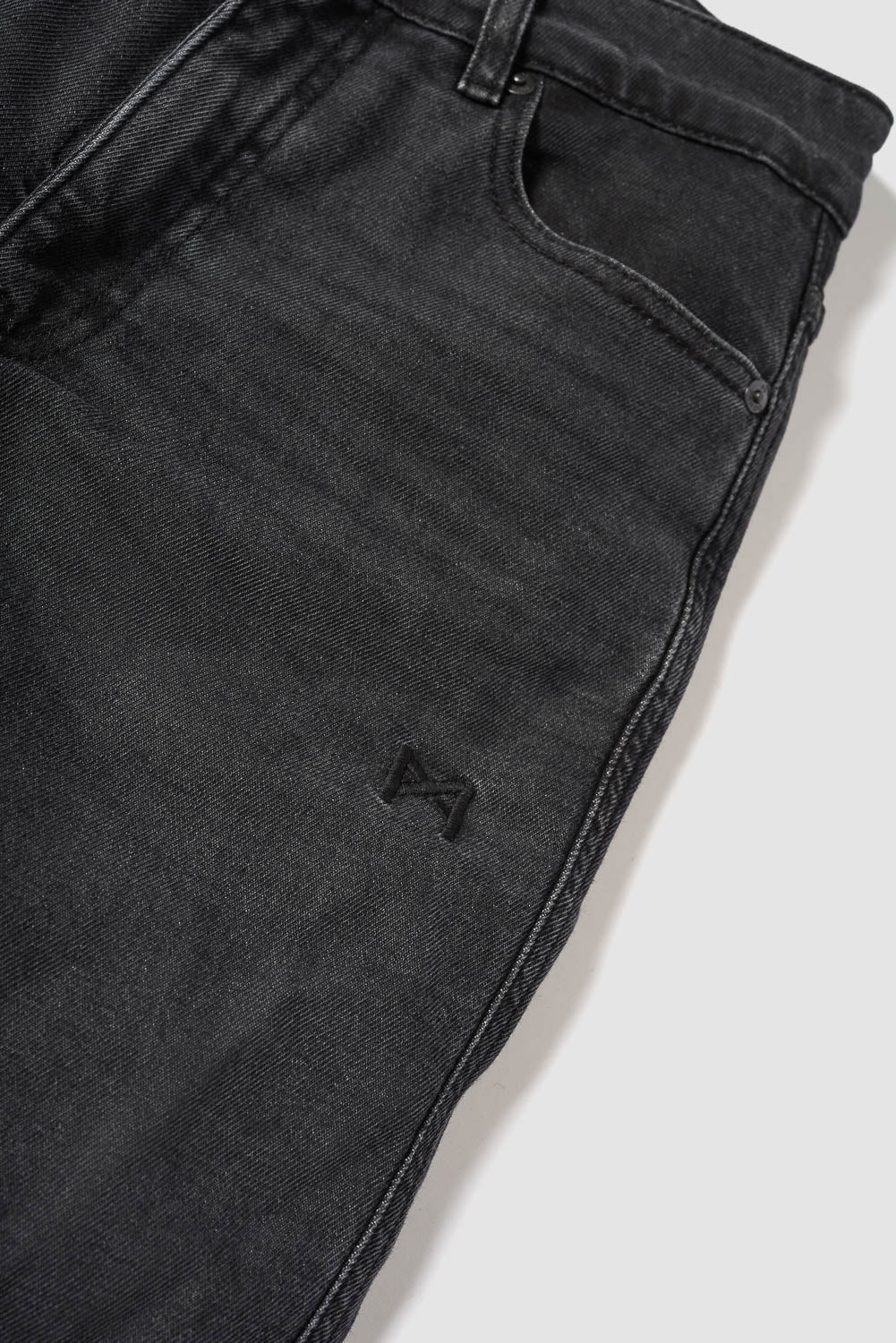 Close-up of black jeans with a brand logo on a white background