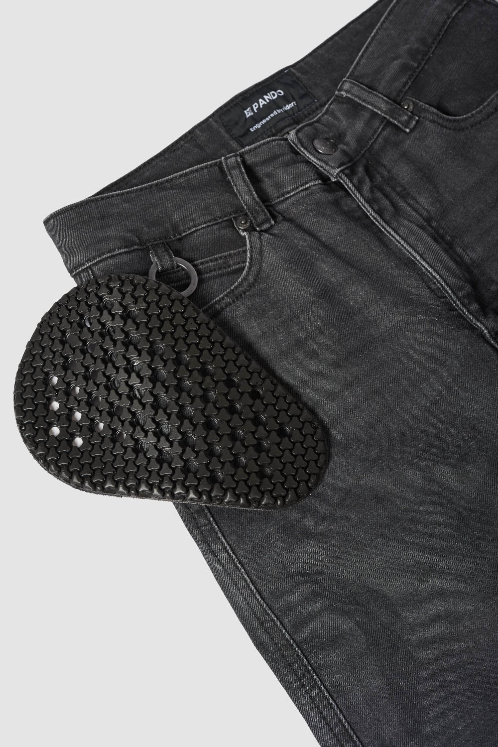 Black textured shoe insert on a pair of black jeans with a visible brand label.