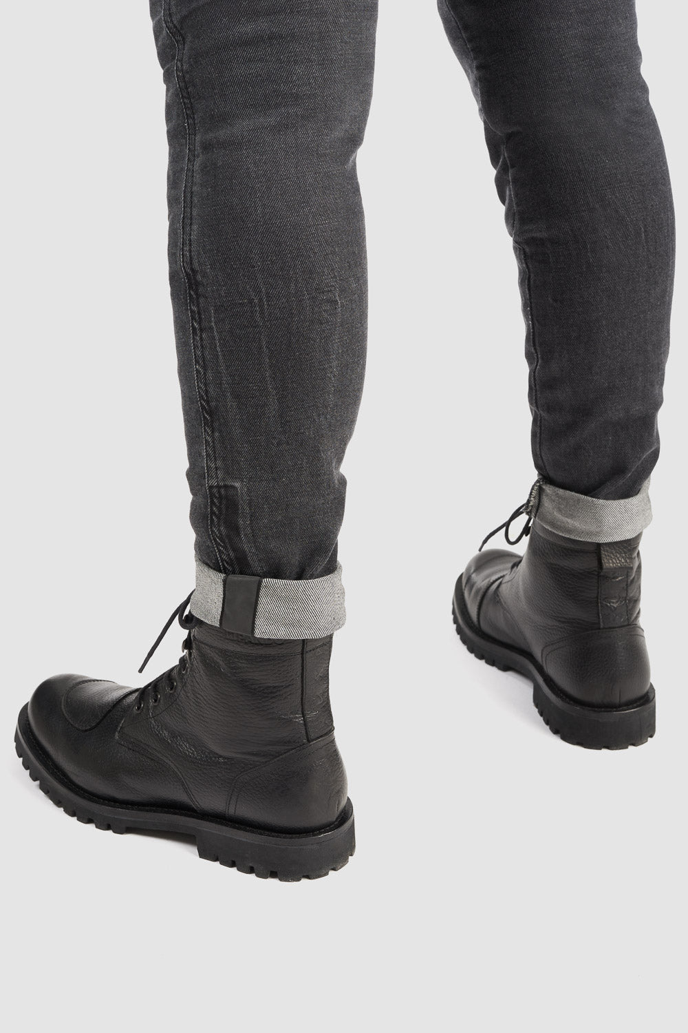 Person wearing black leather boots and gray jeans on a white background
