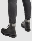 Person wearing black leather boots and gray jeans on a white background