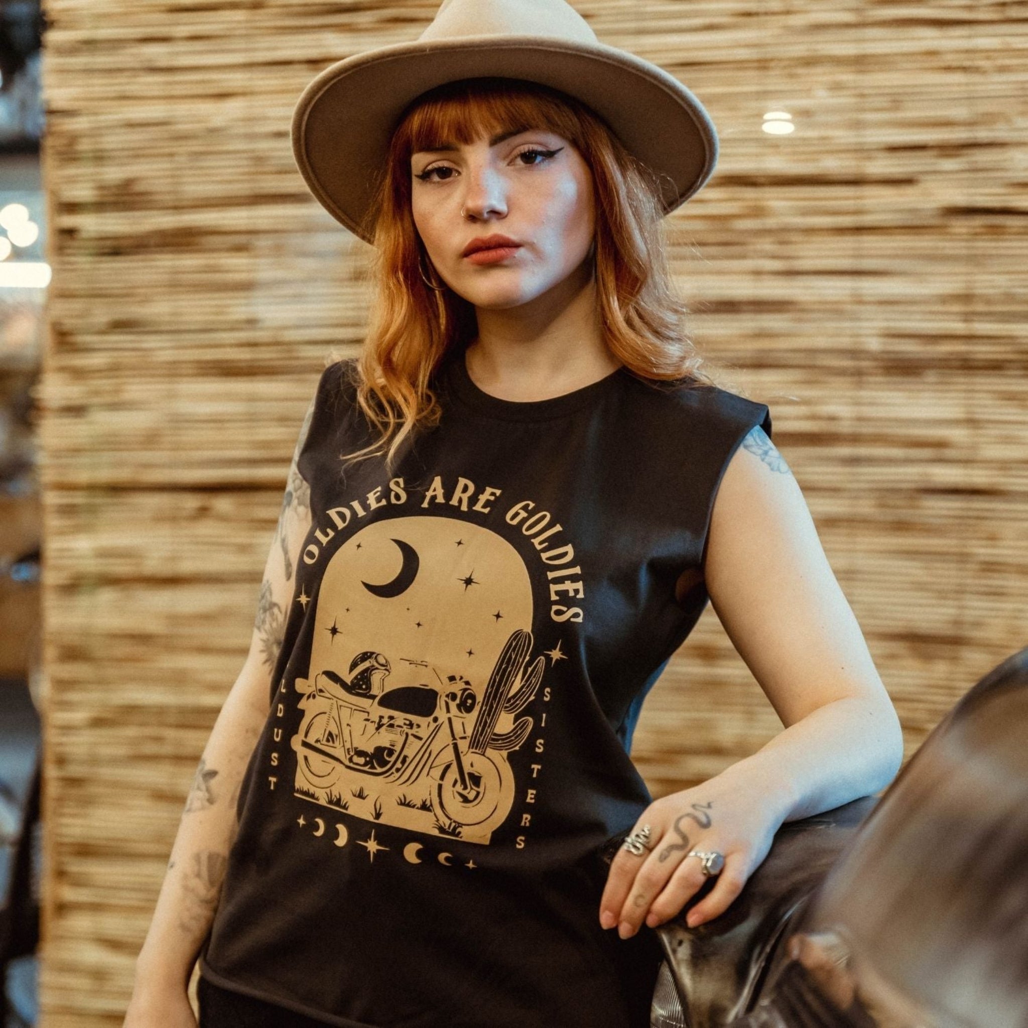 a young woman with a hat wearing off-black tank top with brown motorcycle motive and oldies but goldies text