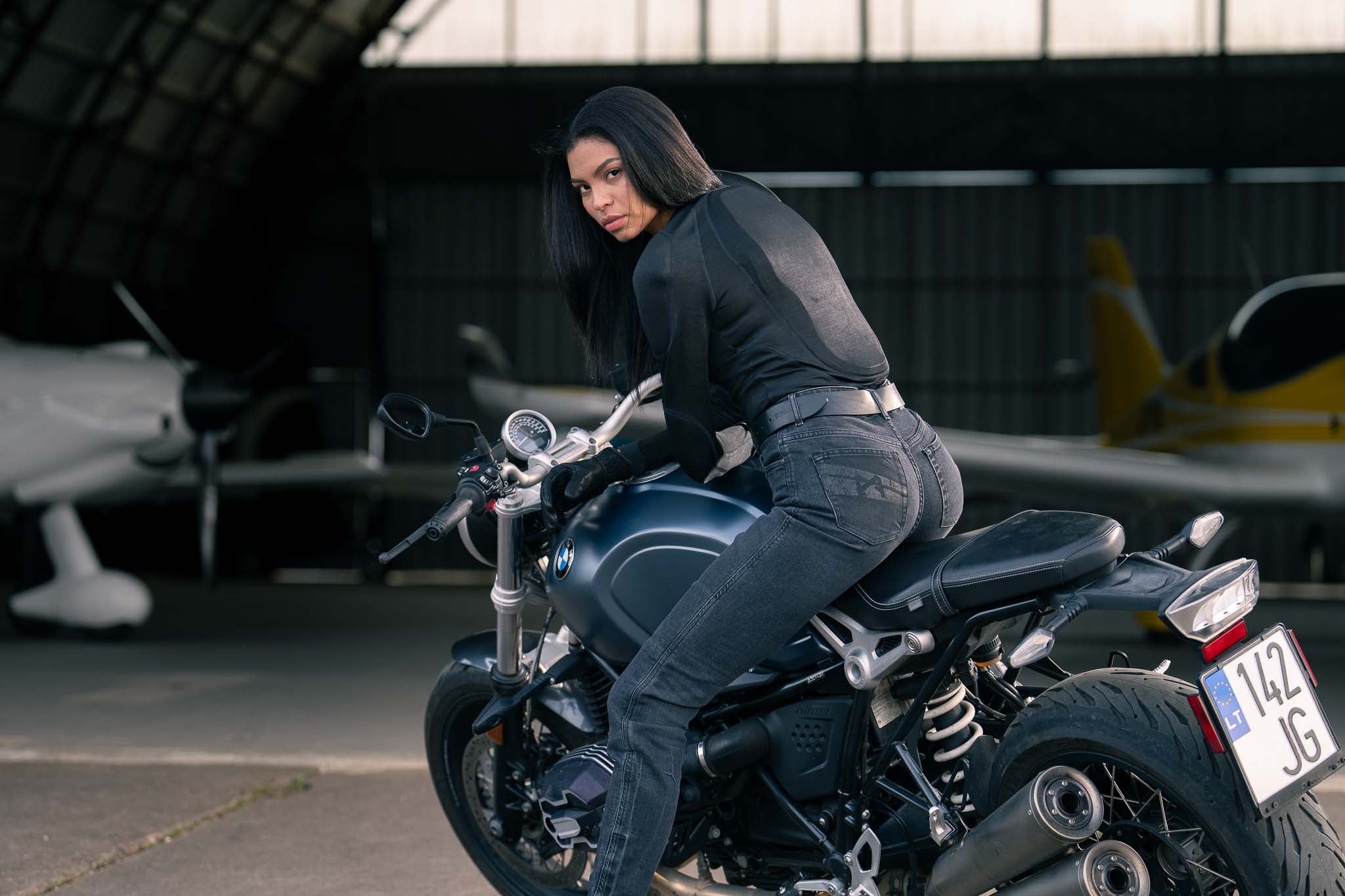 A woman sitting on a motorcycle with airplanes in the background