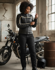 Woman in motorcycle gear standing next to a motorcycle in an industrial setting