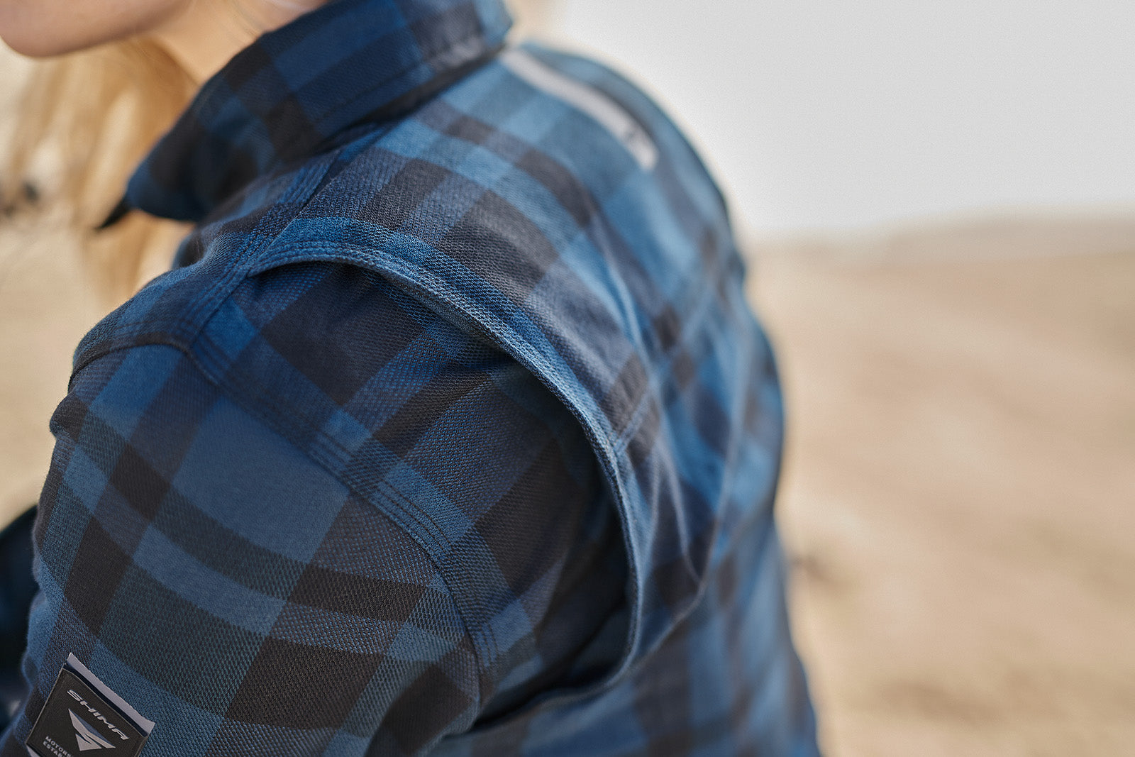 Close-up of a person wearing a blue plaid shirt with a blurred background