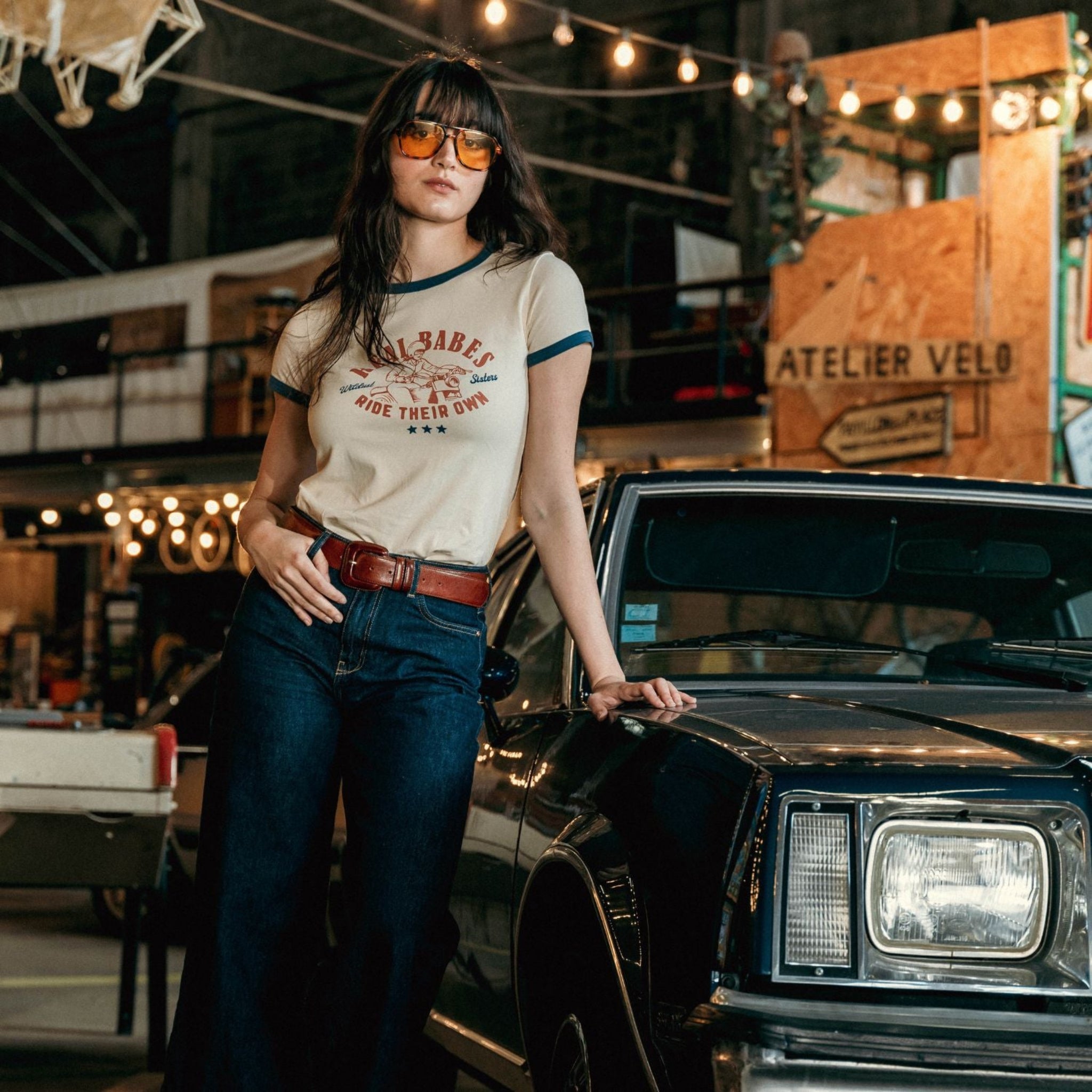 young dark haired woman standing by a retro car and wearing REAL BABES RIDE THEIR OWN retro style t-shirt