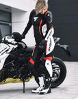 A woman standing next to her motorcycle wearing SHIMA MOTORCYCLE LEATHER suit IN BLACK FLUO, WHITE AND RED FLUO