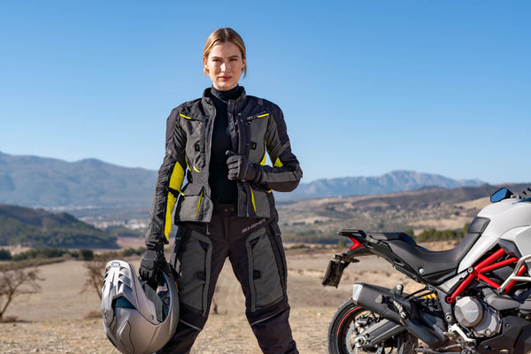 A young woman standing by her motorcycle wearing shima motorcycle touring jacket for women in black/ fluo