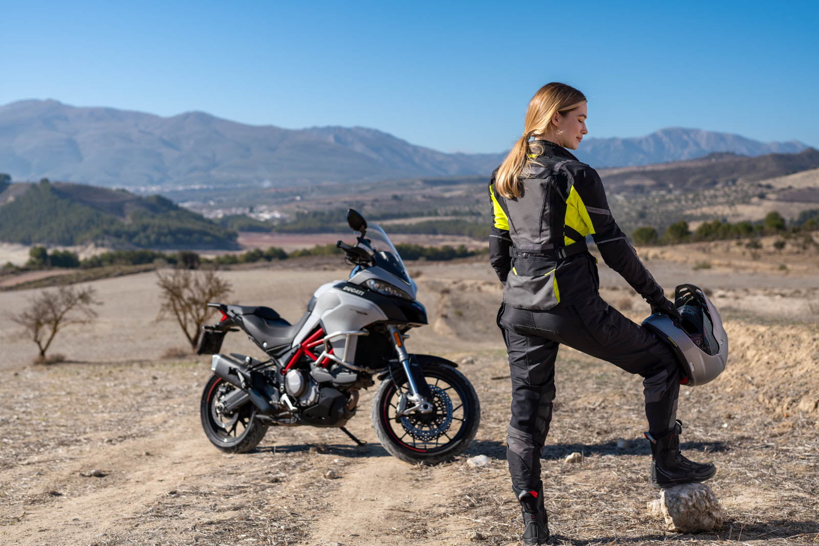 A woman standing by her motorcycle wearing Black SHIMA touring motorcycle pants for women