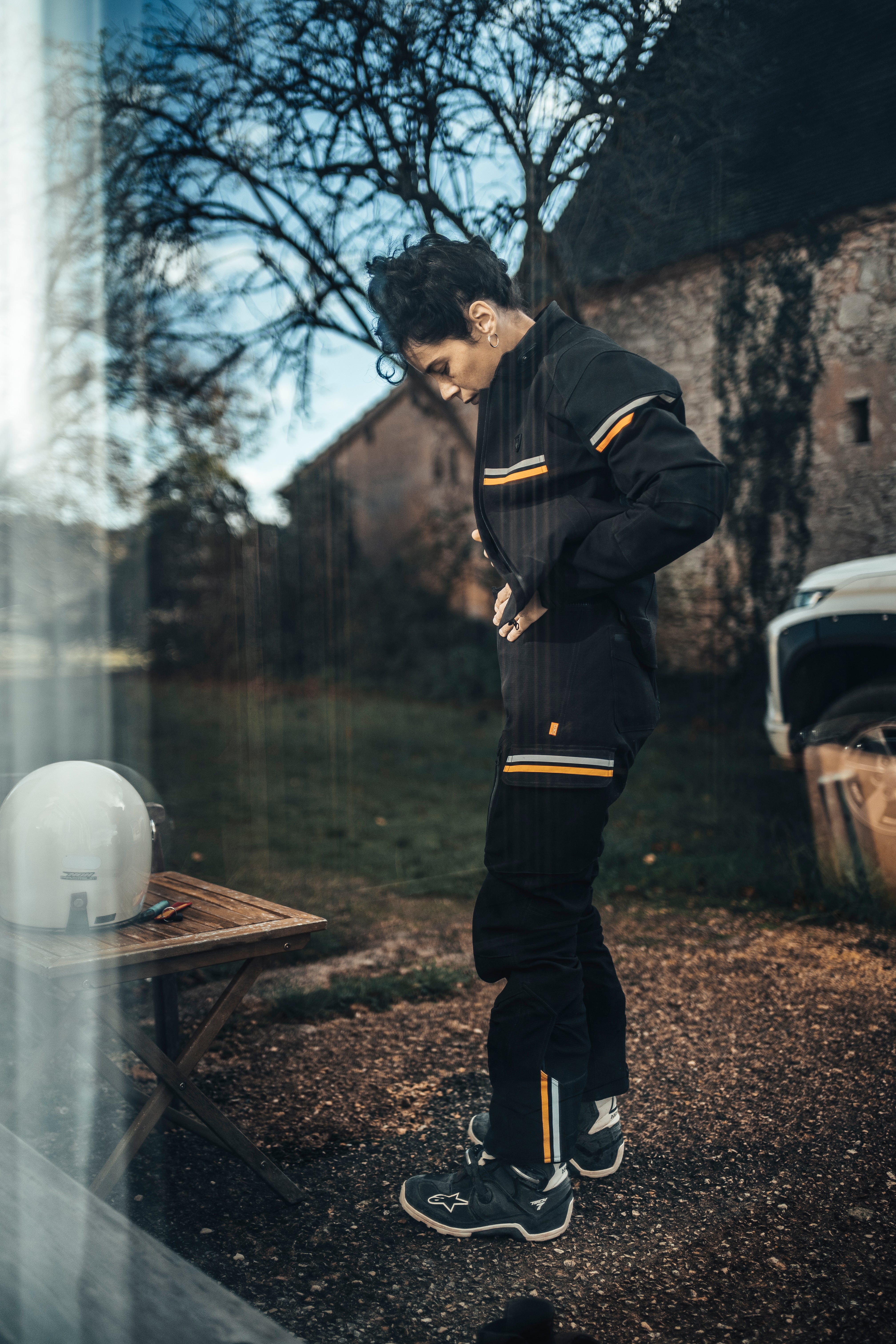 Person wearing a black tracksuit with yellow stripes outdoors near a building.
