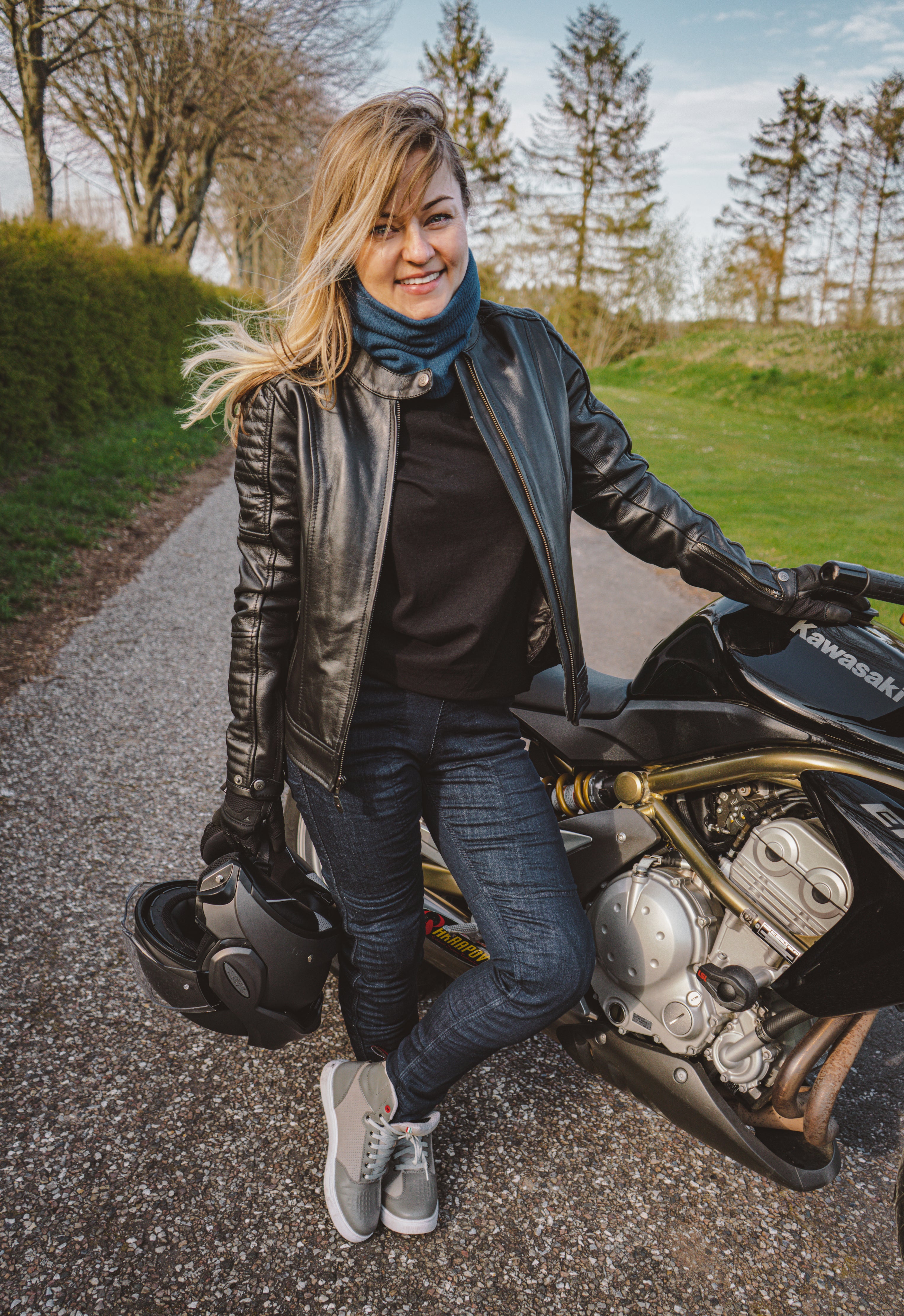 A young woman standing by her Kawasaki motorcycle wearing black leather jacket