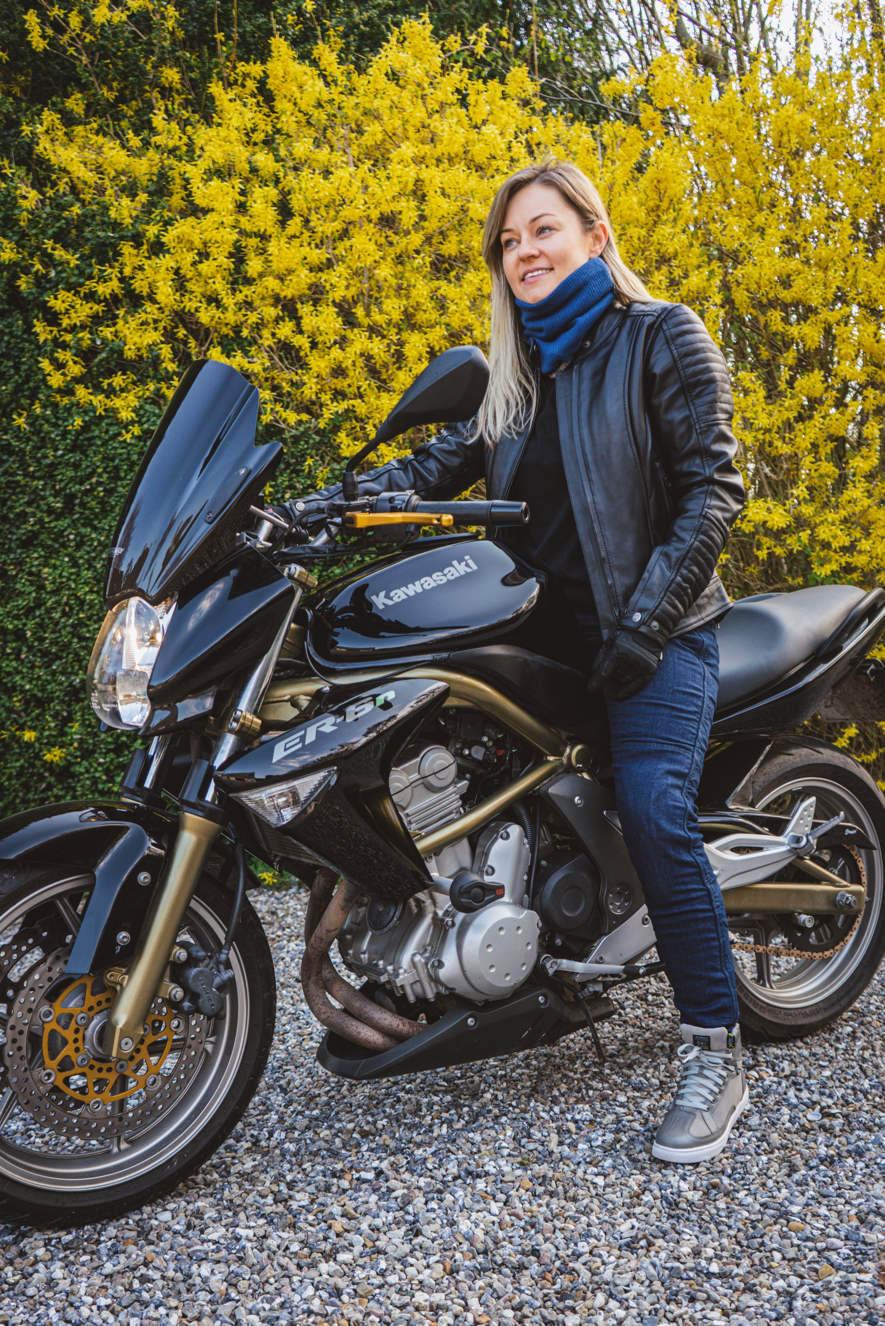 A blond woman on a motorcycle wearing black leather jacket 
