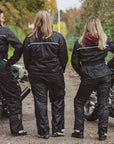 Three women with their motorcycles wearing black rain suits