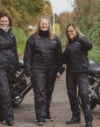 Three women standing by their motorcycles wearing black rain gear
