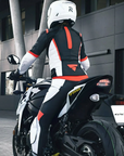 A woman on a motorcycle wearing SHIMA MOTORCYCLE LEATHER suit IN BLACK FLUO, WHITE AND RED FLUO