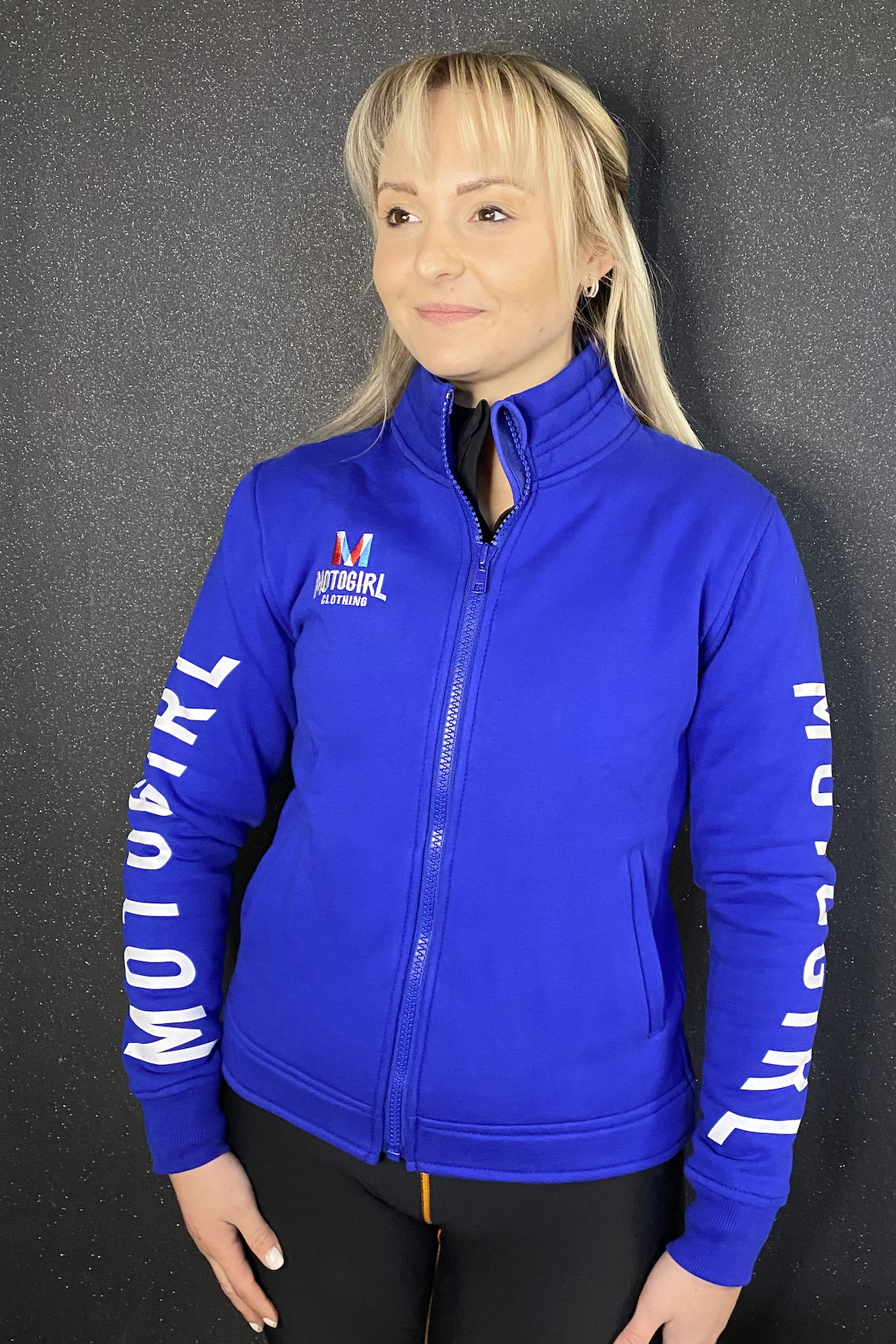 a blond woman wearing Motogirl clothing blue sweatshirt with a front zip
