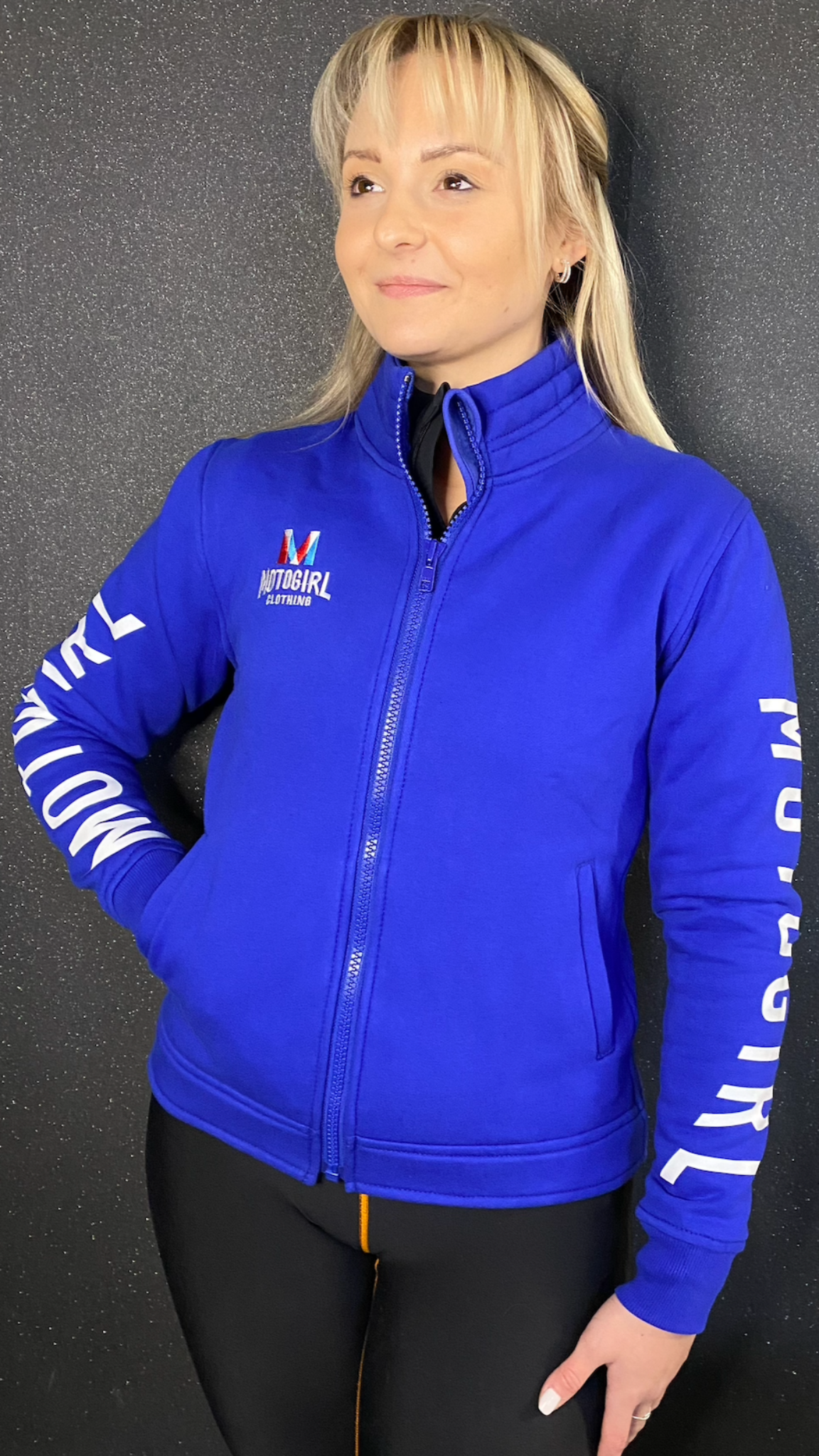 a blond woman wearing Motogirl clothing blue sweatshirt with a front zip