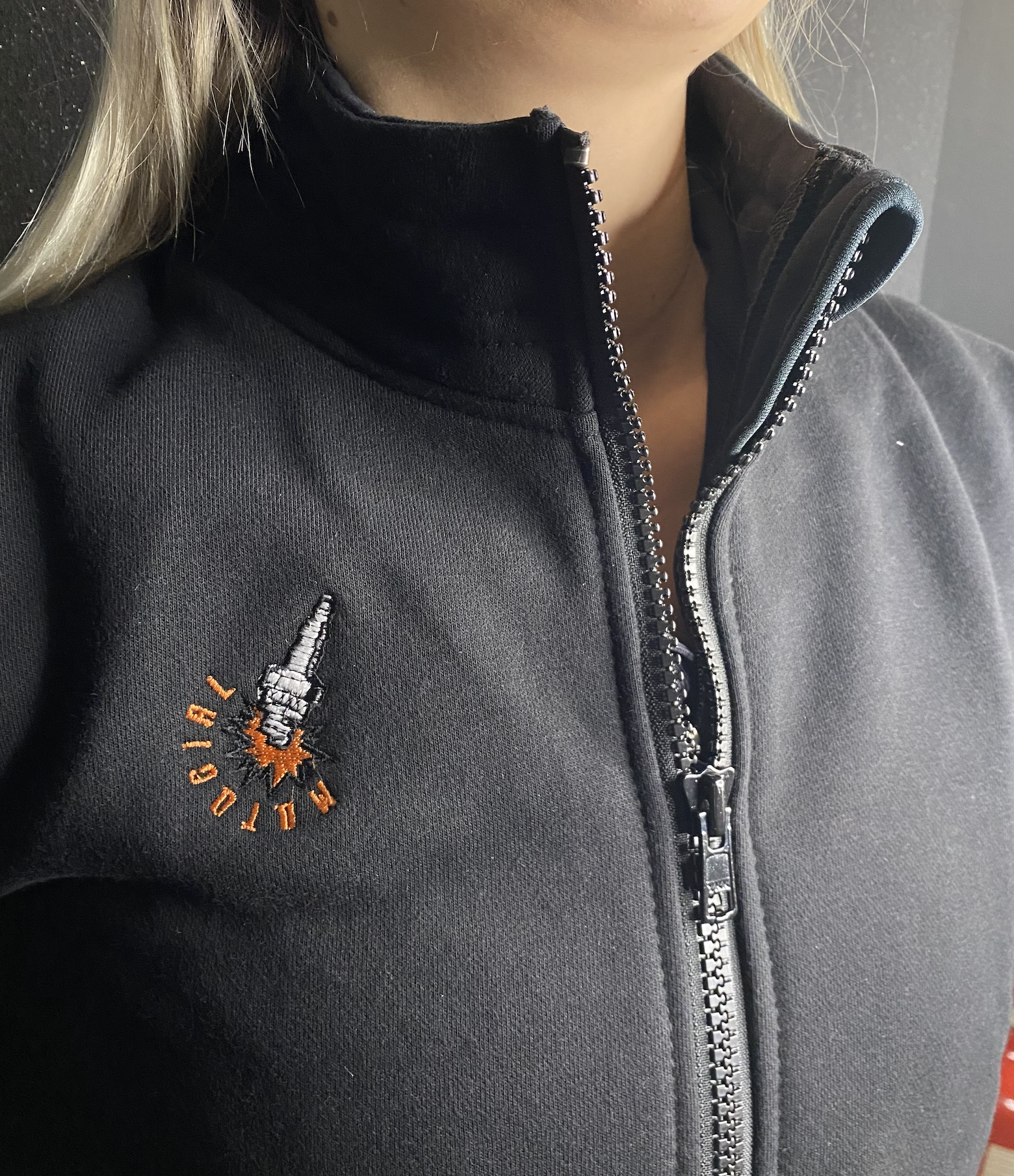 a close up of a woman's neck wearing black sweatshirt with a zip and MotoGirl embroidery 