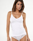 Dark-haired woman wearing a white sleeveless tank top  with bow detail and matching thongs with lace details from Tramonte. 