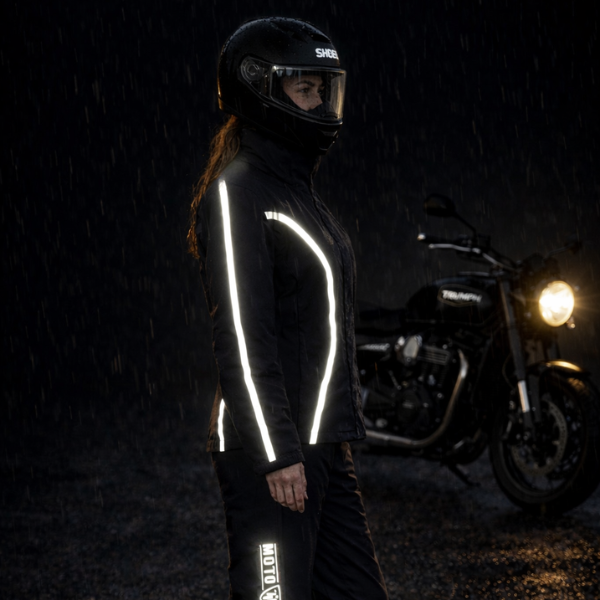 Person wearing a reflective jacket standing next to a motorcycle in the rain.
